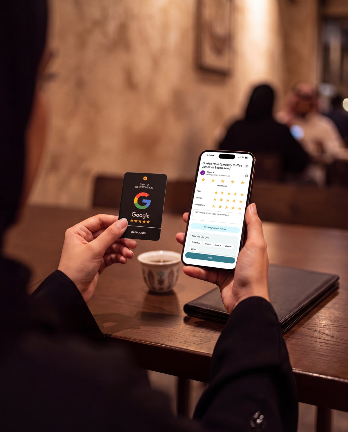 Customer holding the RATECARDS Premium Black Google Review Card in an evening café