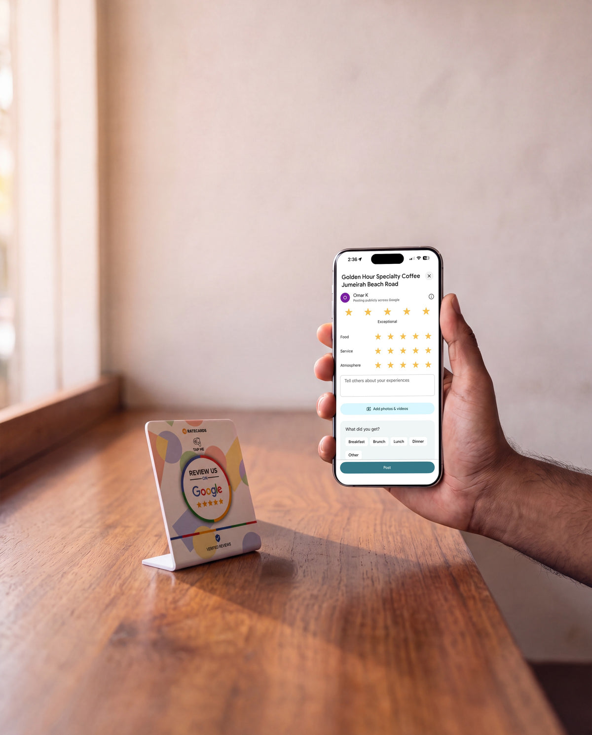 RATECARDS Google Review Stand on a café counter, phone showing the Google review screen after a tap