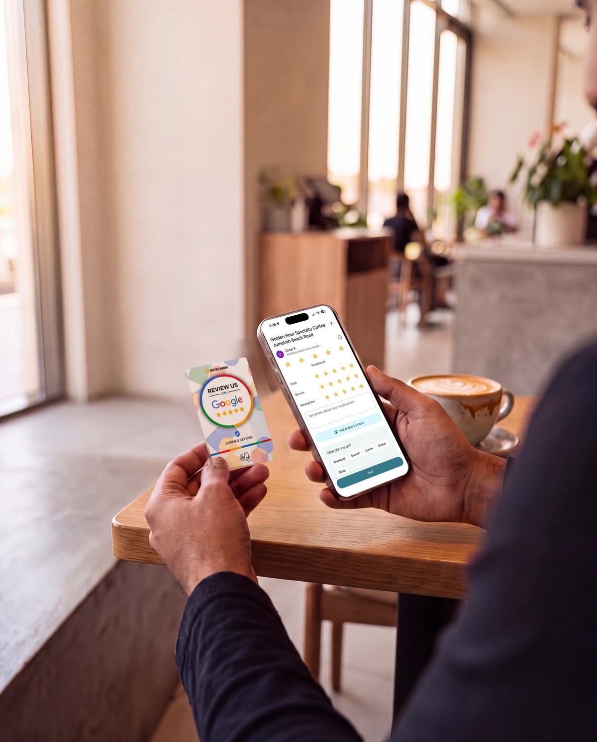 Customer holding a RATECARDS Google Review Card in a café, phone open on the Google review screen